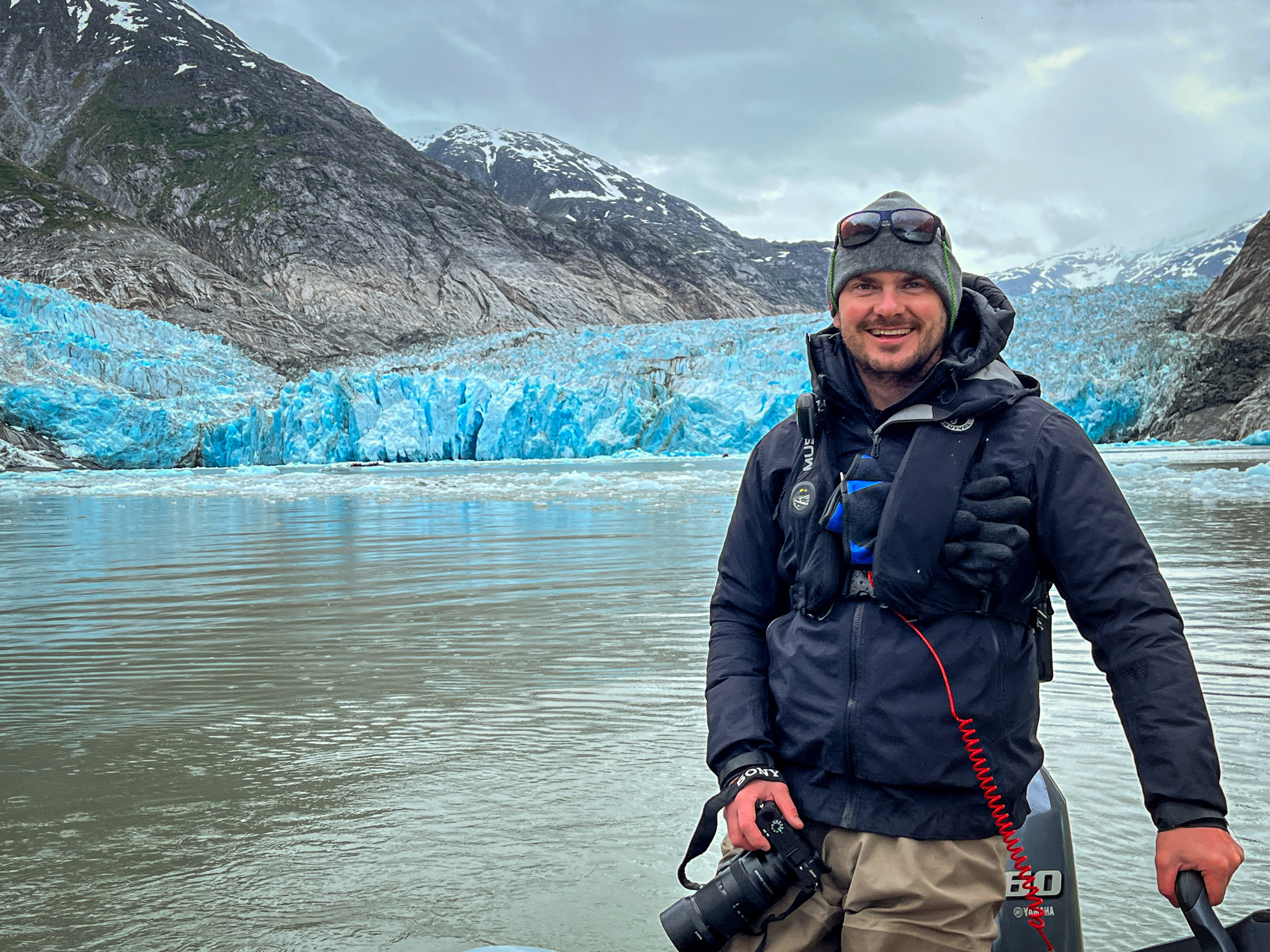 Bryan Bowles, smiling in the foreground of a magnificent glacier, representing his role at Maple Leaf Adventures.